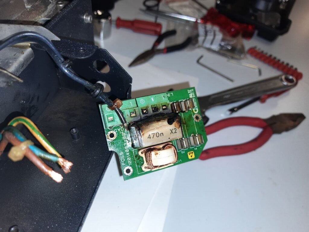 Detalle de un condensador de seguridad RIFA X2 de 470nF agrietado y quemado en una placa de filtro EMI FOSS, con signos de explosión térmica y carbonización en la parte superior.