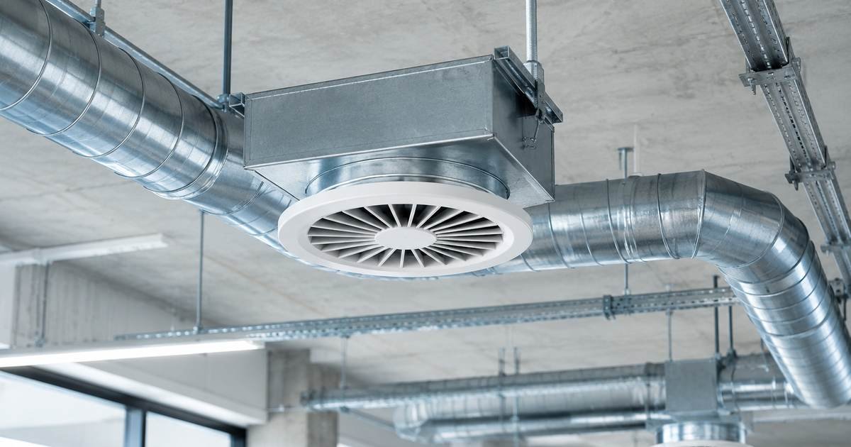 Conductos metálicos y difusor circular de una instalación de ventilación en un edificio comercial